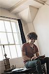 Loft living. A man sitting by a window using a digital tablet.