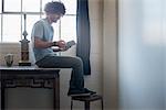 Loft living. A young man sitting on a table using a digital tablet.