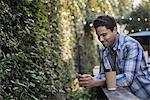 A man sitting at a cafe table outdoors, using his phone.