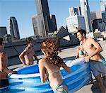 A group of men and women carrying a small inflatable water pool on to a city rooftop