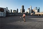 A man standing on a rooftop overlooking the city playing a guitar.