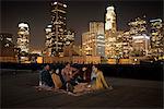 A group of friends gathered on a rooftop overlooking a city lit up at night.