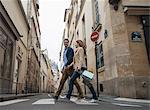 A couple walking along a narrow street in a historic city centre, with shopping bags.