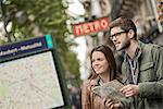 A couple using a street map beside an information sign under a metro sign in a city.