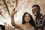 A man and woman in a brightly lit space, a casino entrance, taking a selfy with a smart phone.