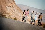 A group of people walking in a line in open desert country, carrying their cases, on a road trip.