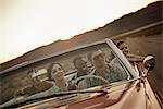 A group of friends in a red open top convertable classic car on a road trip.