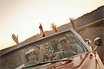 A group of friends in a red open top convertable classic car on a road trip.