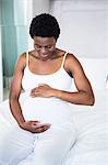 Smiling pregnant woman sitting on her bed