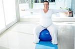 Pregnant woman with arms stretched exercising with ball