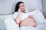 Pregnant woman phoning while lying on bed