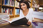 Portrait of female student holding book while lying on floor