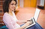 Pretty student using her laptop in hallway