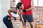 Muscular woman lifting dumbbell with her trainer