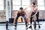 Female trainer helping fit man lifting barbell