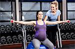 Pregnant woman doing some exercising helped by trainer
