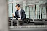 A working day. Businessman in a work suit and tie sitting checking his phone.