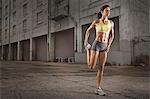 A woman in running gear, crop top and shorts, stretching her body and preparing for a run, or cooling down after exercise.