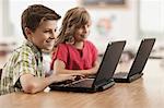 Two children seated at desks in class using laptop computers.