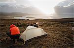 Two men holding and putting up a small tent in open space. Wild camping.