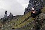 A man on a slope with a backdrop of rock pinnacles on the skyline, a dramatic windswept landscape.