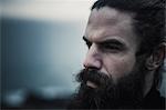 A man with full  beard and moustache and black hair scrapped back from his face.