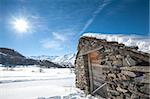 Remote alpine mountain hut on a slope in the sunlight covered with snow