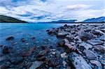 Beautiful dramatic sunset over the incredibly blue lake Tekapo with mountains, Southern Alps, on the horizon. New Zealand