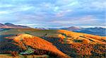 Autumn evening plateau landscape with lust golden sunlight on mountains and pink evening glow in sky.