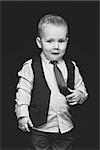 Handsome shy little boy in business suit with emotional expression on face touching his blue tie. Over dark background.