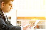 Asian Indian business people using tablet pc at cafe, relaxing with a cup of coffee. India male business man, modern office building with sunlight as background.