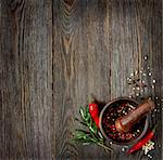 Fresh rosemary with chili  and peppercorns in mortar on wooden background.