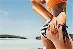 Sandy ass of a young beautiful sporty woman in striped black and white bikini on the tropical ocean shore background. Outdoor lifestyle picture on a hot sunny summer day.