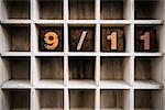 The word "9/11" written in vintage ink stained wooden letterpress type in a partitioned printer's drawer.