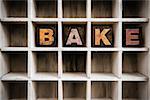 The word "BAKE" written in vintage ink stained wooden letterpress type in a partitioned printer's drawer.