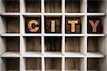 The word "CITY" written in vintage ink stained wooden letterpress type in a partitioned printer's drawer.