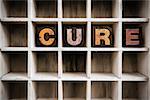 The word "CURE" written in vintage ink stained wooden letterpress type in a partitioned printer's drawer.