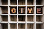 The word "GIVE" written in vintage ink stained wooden letterpress type in a partitioned printer's drawer.
