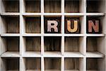 The word "RUN" written in vintage ink stained wooden letterpress type in a partitioned printer's drawer.