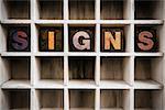 The word "SIGNS" written in vintage ink stained wooden letterpress type in a partitioned printer's drawer.