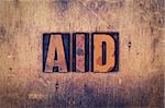 The word "Aid" written in dirty vintage letterpress type on a aged wooden background.