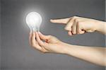 A finger pointing to a glowing light bulb in a hand