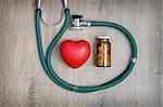 Overhead view of a stethoscope, a glass of pills and a red heart shape