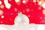 white decorative christmas ball on snow against red festive background