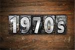 The word "1970s" written in vintage metal letterpress type on an aged wooden background.