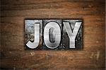 The word "Joy" written in vintage metal letterpress type on an aged wooden background.