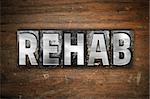 The word "Rehab" written in vintage metal letterpress type on an aged wooden background.