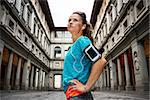 Now it is time to invest in your body and no matter you are at hometown or traveling. Young sporty female with headset staying in front of Uffizi gallery and listening music