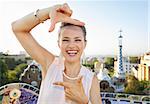 Refreshing promenade in unique Park Guell style in Barcelona, Spain. Happy young woman tourist framing with hands in Park Guell, Barcelona, Spain