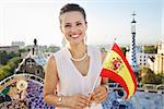 Refreshing promenade in unique Park Guell style in Barcelona, Spain. Portrait of smiling young woman tourist with Spain flag in Park Guell, Barcelona, Spain